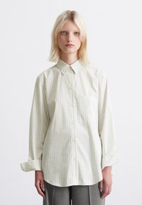 Striped button-up shirt in light cream with vertical thin lines, collar, long sleeves, and front pocket; smooth fabric texture.
