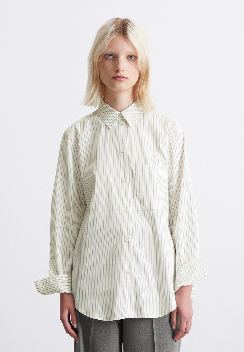 Striped button-up shirt in light cream with vertical thin lines, collar, long sleeves, and front pocket; smooth fabric texture.