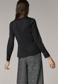 Maglietta nera a maniche lunghe con una silhouette aderente, caratterizzata da una texture liscia e una lucentezza sottile, abbinata a pantaloni grigi con fantasia.
