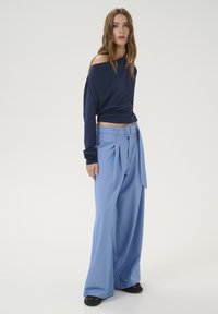 Marinblus med lång ärm och off-shoulder design, tillsammans med ljusblå vida pleated byxor med bälte och texturerad tyg.