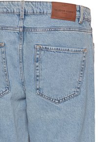 Lyseblå cowboybukser i denim med baglommer og en brun læderlabel med teksten "The Denim Journey by Isolid."