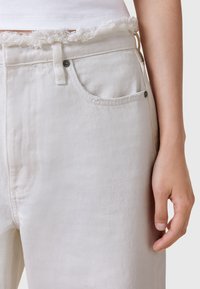 Pantalones de mezclilla blancos con una cintura deshilachada, con un bolsillo en el lado derecho y un diseño clásico de cinco bolsillos. Tejido texturizado.