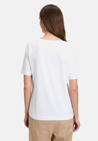 T-shirt blanc à manches courtes avec un col rond et une texture lisse, associé à un pantalon beige. Design simple, sans motifs visibles.