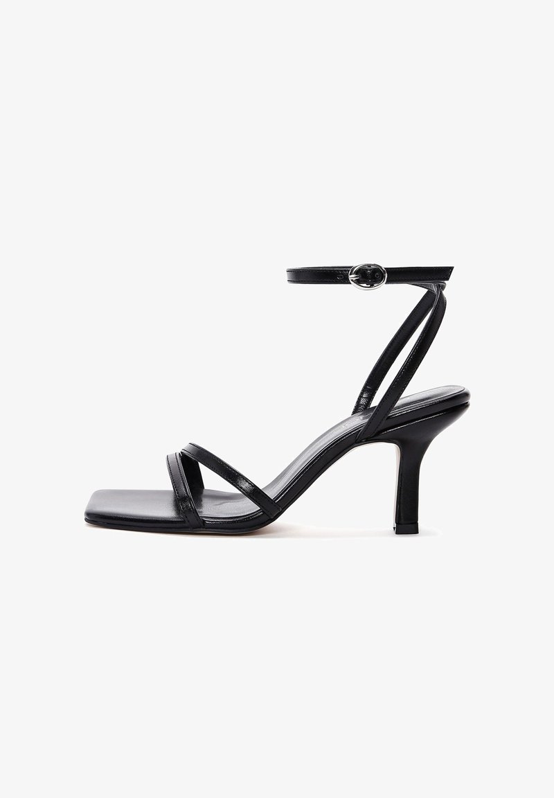 Sandale à talons hauts noire avec un bout carré, dotée de deux fines brides, d'une bride de cheville avec boucle et d'une finition brillante.