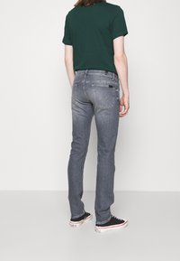 Jeans in denim grigio con una vestibilità slim, caratterizzati da cuciture sottili, tasche posteriori e una vita standard. Indossati con una t-shirt verde e sneakers nere.