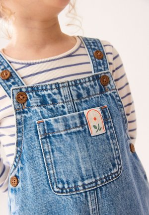 Kind trägt blaue Denim-Latzhose mit braunen Knöpfen und ein gestreiftes langärmeliges Shirt, Teilansicht vom Hals bis zur Taille.