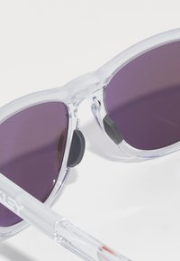 Occhiali da sole in plastica trasparente con lenti viola, dotati di cuscinetti nasali in gomma nera e un design elegante e moderno.