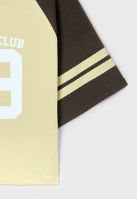 T-shirt de sport à manches courtes avec devant beige, manche marron avec deux bandes beiges, et grand numéro huit blanc avec texte partiel au-dessus.