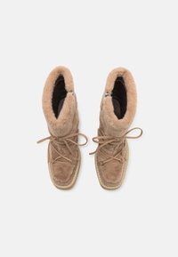 Botas tobilleras marrones esponjosas hechas de suave ante, con cierre de cordones y diseño de punta redonda, y un interior texturizado y cálido.