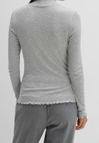 Grå räfflad långärmad topp med en mock neck, med rå kant och åtsittande silhuett, kombinerad med grå byxor.