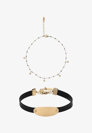Brățară delicată din lanț cu mărgele aurii și negre, cu bile mici atârnânde, asortată cu un colier choker din piele neagră cu o placă ovală aurie.