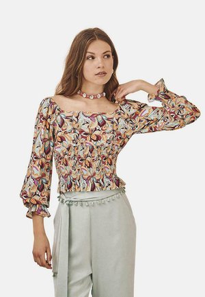 Blusa floral multicolorida con mangas largas abullonadas, cintura fruncida y escote redondeado, combinada con pantalones tapered de color verde claro con un acabado de borlas.