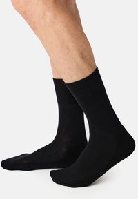 Calcetines de algodón negros con puños acanalados y textura suave, con una longitud hasta la mitad de la pantorrilla y un diseño de puntera sin costuras.