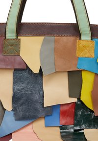 Patchwork læder tote med forskellige farver, herunder brun, blå, grøn og gul. Har særprægede teksturer og synlige syninger.