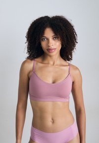 Soutien-gorge seamless rose clair avec de fines bretelles, en tissu doux et à la texture lisse, associé à un bas de bikini assorti. Détails de conception minimalistes.