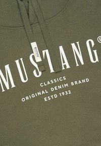Felpa verde oliva con testo bianco che recita "MUSTANG CLASSICS ORIGINAL DENIM BRAND ESTD 1932." Dotata di coulisse e un'etichetta con il marchio.