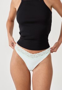 Culotte de bikini avec dentelle en vert menthe clair, avec un corps lisse. Associée à un débardeur noir à côtes. Accent sur les détails en dentelle.