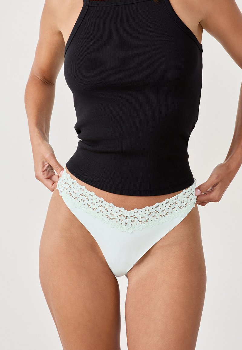 Culotte de bikini avec dentelle en vert menthe clair, avec un corps lisse. Associée à un débardeur noir à côtes. Accent sur les détails en dentelle.
