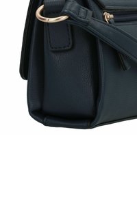 Sac à main en cuir marine avec une forme structurée, présentant une texture lisse, une fermeture éclair et un accent métallique circulaire sur la bandoulière.