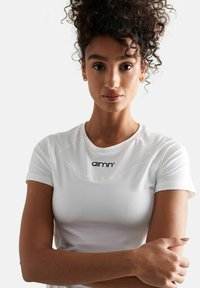Witte sportieve T-shirt met korte mouwen, voorzien van een ronde halslijn en een zwart "aimn" logo op de borst. Glad materiaal en een getailleerd ontwerp.