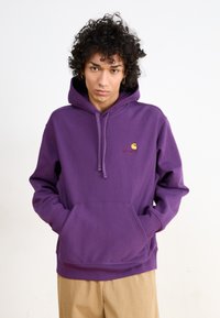 Lilla cotton hoodie med en frontkangaroo-lomme, justerbar snoretræk-hætte og et lille gult logo på brystet.
