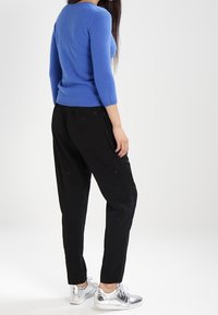 Blå, figurnära, långärmad tröja med ribbat halsband som kombineras med svarta, löst sittande byxor och silvriga, lätta sneakers.