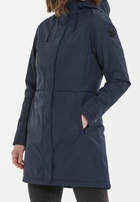 Laivastonsininen vedenpitävä parka hupulla, elastisella nyörillä, etutaskuilla ja nappisuljennalla. Sisältää brändätyn tarran hihassa.