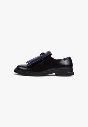 Black leather shoe with rounded toe, flat sole, and decorative blue tassel. Smooth texture and minimalist design with subtle logo detail.