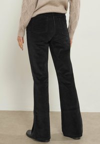 Zwarte fluwelen uitlopende broek met verticale ribbels, vijf zakken en een middelhoge tailleband, gecombineerd met een beige gebreide trui.