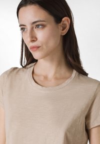 T-shirt beige a maniche corte realizzato in tessuto morbido, con colletto rotondo e vestibilità rilassata, caratterizzato da una texture sottile e cuciture minime.