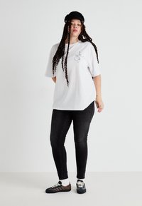 Bílé oversize tričko s liniovým kreslením, spárované s černými skinny džíny a vícebarevnými teniskami. Také obsahuje černou kšiltovku.
