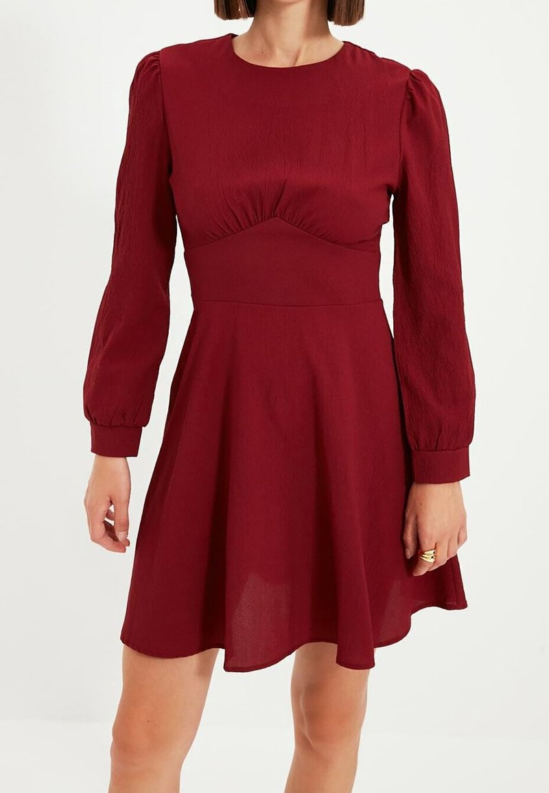 Burgundy klänning med figursydd överdel, puffärmar och utsvängd kjol. Tillverkad av strukturerad tyg med en slät finish.