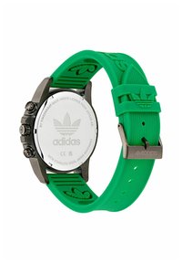 Grön gummirem-klocka med svart rostfritt stalhus, tre knappar och ingraverad logotyp på baksidan. Har ett strukturerat rem med varumärkesemblem.