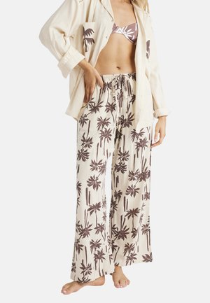 Linnenoutfit met een lichtbeige shirt met palmbomenprint en bruine, loszittende broek met een vergelijkbare palmbomenprint.