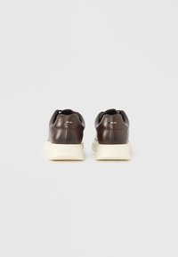 Baskets en cuir marron à profil bas, semelles en caoutchouc crème et lacets courts. L'arrière présente un détail de logo discret près du talon.