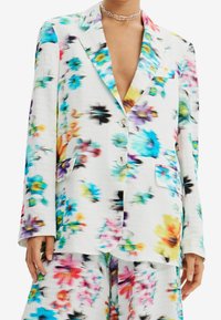 Kwiatowa marynarka w białym kolorze z kolorowymi wzorami w odcieniach niebieskiego, różowego, żółtego i czarnego. Posiada kołnierz z wycięciem i zapięcie na guzik; lekki materiał.