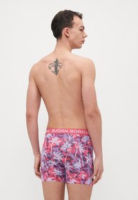 Férfi boxer alsónemű, rózsaszín és lila pálmafa mintával, kontrasztos rózsaszín derékrésszel, amelyen a "BJÖRN BORG" felirat található. Sima anyag, testhezálló kivitel.