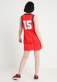 Maillot de basketball rouge avec un grand numéro 15 blanc, doté d'un col côtelé et d'une texture en mesh. Assorti à des chaussures sombres.