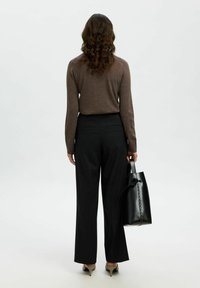 Maglietta marrone a maniche lunghe, pantaloni neri a gamba larga e una borsa nera con dettaglio a fiocco, vista da dietro. Texture liscia e design sartoriale.