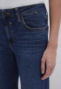 Dark blue denim jeans with a classic five-pocket design. Features orange stitching, a button closure, and a slim fit around the waist.