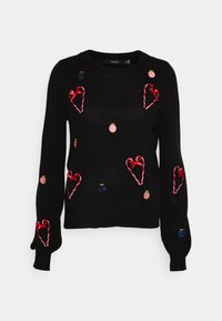 Svart tröja med färgglada broderade hjärtan, godisträn och cirkulära dekorationer. Den har långa ärmar och rund halsringning.