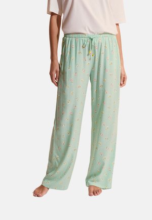 Lichtgroene pyjamabroek met kleine bloemenprint en een taille met trekkoord, gedragen door een persoon die op blote voeten staat tegen een witte achtergrond.