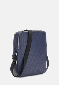 Mörkblå axelremsväska med texturerat mönster, dragkedjeslutning och justerbar svart rem. Fyrkantig form, syntetiskt material, modern design.