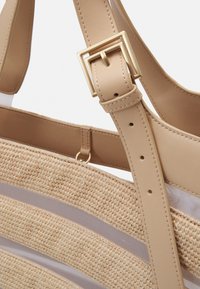 Tan kudontasku, jossa on rakenteellinen olki-tyylinen päällinen, sileät nahkaiset hihnat ja kullanvärinen solki-säätöyksityiskohta.