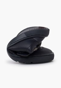 Chaussure noire flexible pliée en deux, montrant la semelle en caoutchouc et la tige en cuir souple, mettant en avant son design pliable et compact.