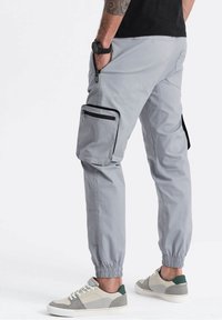 Grijze cargobroek met elastische boorden, met ritssluitingen aan de zijzakken en een gestructureerde afwerking. Gecombineerd met lichte sneakers met groene accenten.