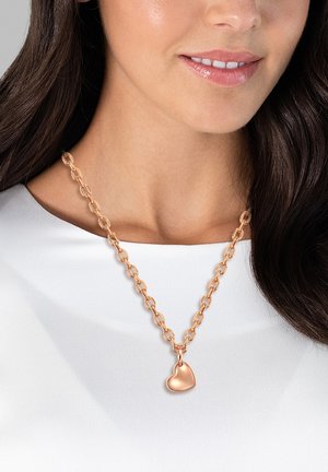 Rosen guld halskæde med et kædedesign og en hjerteformet vedhæng, hviler på en hvid tøjbaggrund.