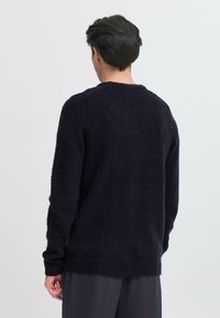 Pulover tricotat bleumarin cu un finisaj texturat, guler rotund, manșete și tiv nervurat. Croială lejeră, prezentat din spate, asortat cu pantaloni negri.