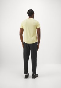 Gul kortärmad skjorta med rundad nederkant, kombinerad med svarta slim-fit byxor med sidofickor och dragkedjor. Svarta sportskor fulländar looken.