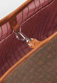 Sac à main marron avec un extérieur texturé, une doublure intérieure rose avec de fines rayures noires, et un clip en métal argenté pour attacher la sangle.